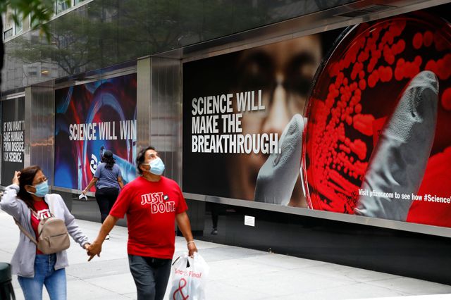 People wearing masks walk past signs outside the headquarters of the pharmaceutical company Pfizer in New York City.